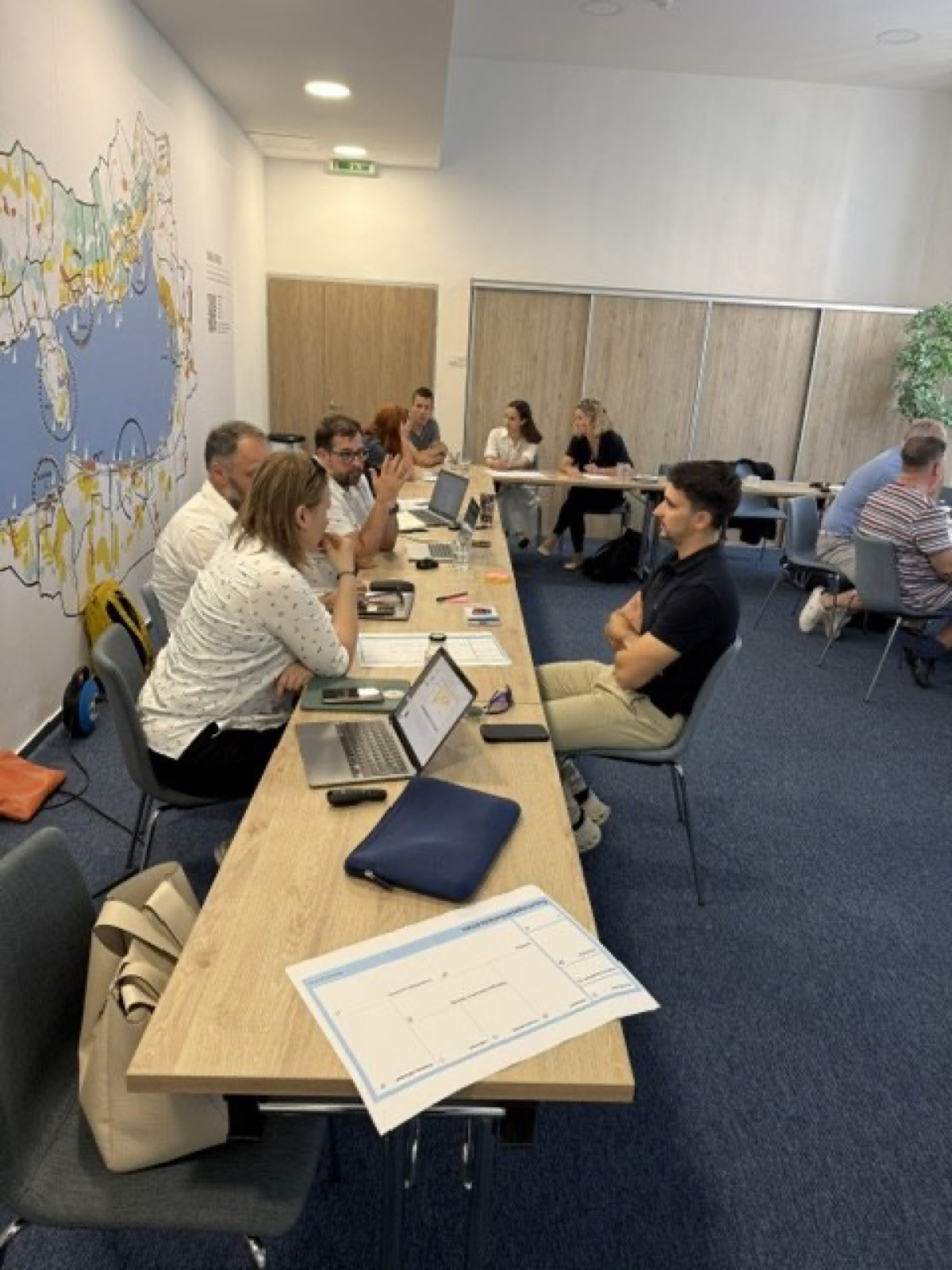 01: Adam Schmutz giving a talk on package pricing at VisitBalaton365's Keszthely training center; in the foreground the “Package creation” canvas with participants' notes. 02: The Keszthely training room with the Lake Balaton map on the wall; participants at the two-day workshop, the title slide on the screen. 03: Small-group work next to the VisitBalaton365 banner and the projected canvas template. 04: Participants following a package example on the projector. 05: The Keszthely training room from above, participants at the U-shaped tables in front of the Lake Balaton map wall. 06: A small group working together on the package canvas. 07: Participants working over the package-planning template at the long table. 08: A lively discussion in a four-person group. 09: Workshop participants in a small-group consultation with notes and a canvas. 10: Participants at the training room table in front of the Lake Balaton map.