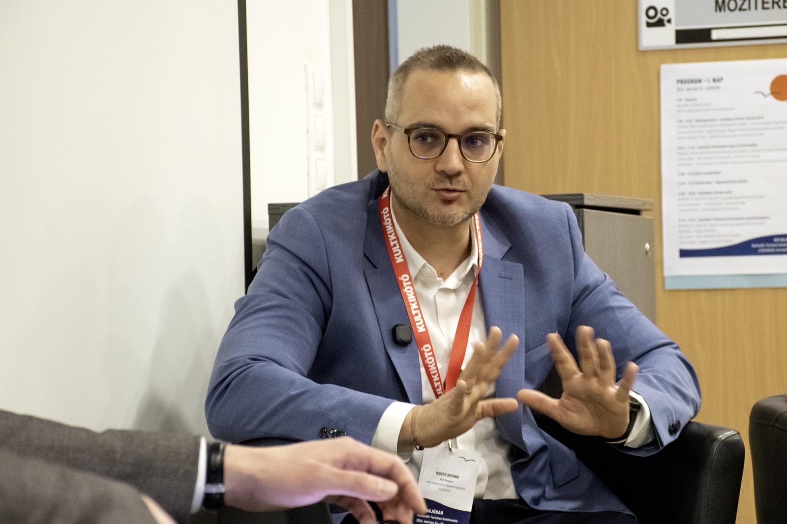 Adam Schmutz on the panel of the KULTKIKÖTŐ conference (Balatonföldvár, 2026) | Adam Schmutz gesturing while speaking on the KULTKIKÖTŐ conference panel | Adam Schmutz and Botond Boros (Visit Hungary) discussing tourism innovation at the KULTKIKÖTŐ conference | Botond Boros, Visit Hungary expert, on the panel at the KULTKIKÖTŐ conference | The audience of the KULTKIKÖTŐ conference during the panel | A question from the audience at the KULTKIKÖTŐ conference panel | KULTKIKÖTŐ – In the Same Boat Cultural Tourism Conference 2026 – conference badges