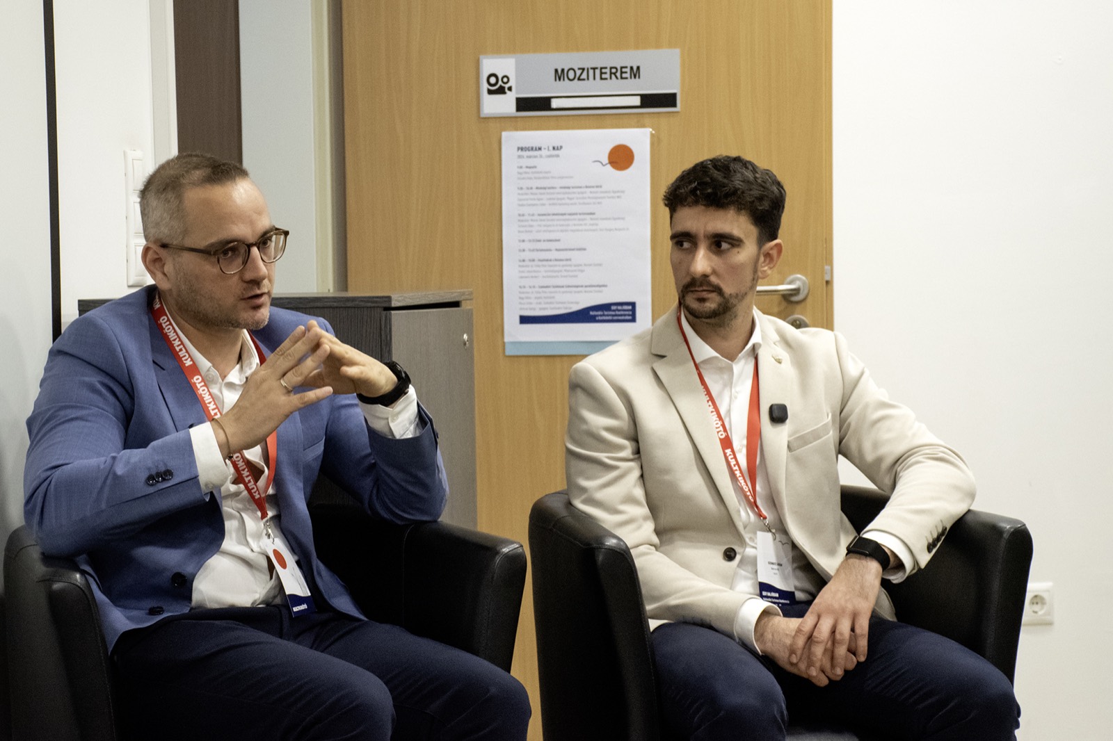 Adam Schmutz on the panel of the KULTKIKÖTŐ conference (Balatonföldvár, 2026) | Adam Schmutz gesturing while speaking on the KULTKIKÖTŐ conference panel | Adam Schmutz and Botond Boros (Visit Hungary) discussing tourism innovation at the KULTKIKÖTŐ conference | Botond Boros, Visit Hungary expert, on the panel at the KULTKIKÖTŐ conference | The audience of the KULTKIKÖTŐ conference during the panel | A question from the audience at the KULTKIKÖTŐ conference panel | KULTKIKÖTŐ – In the Same Boat Cultural Tourism Conference 2026 – conference badges